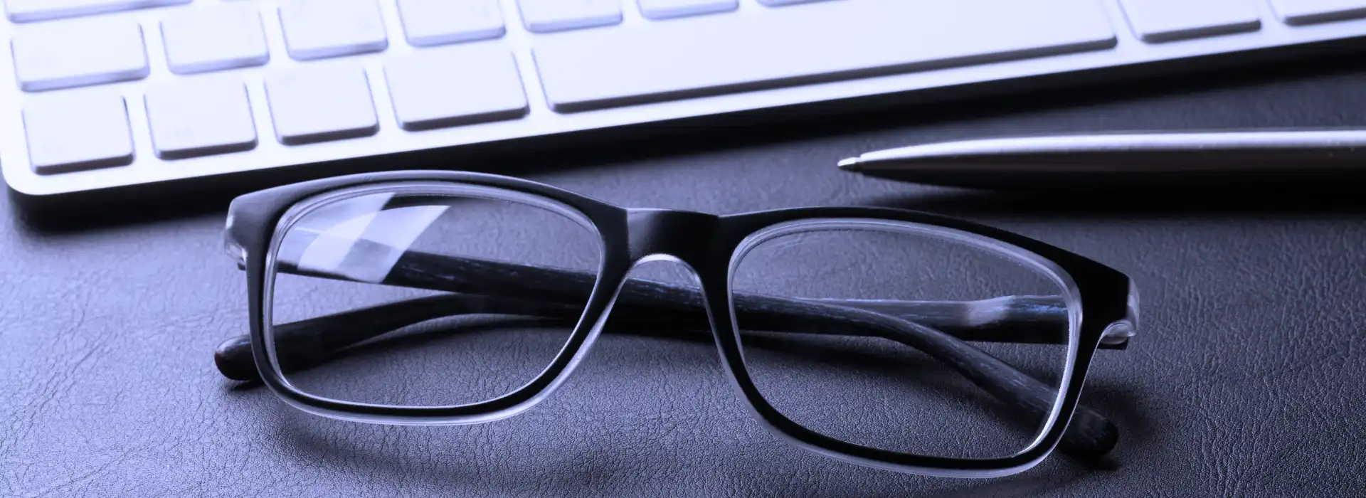 Datorbrilles novietotas pie datora klaviatūras un pildspalvas